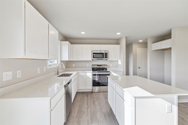 2009 White Oak Ln, Granger, IA 50109 - kitchen with stainless steel appliances, a sink, light wood-style floors, a center island, and white cabinetry