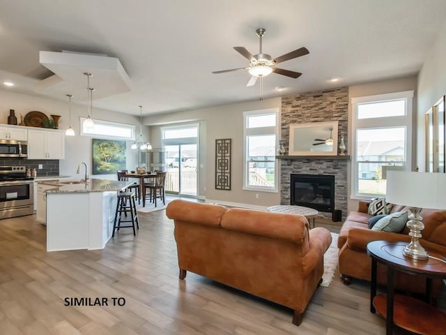 living room featuring a stone fireplace, ceiling fan, sink, and light wood-type flooring