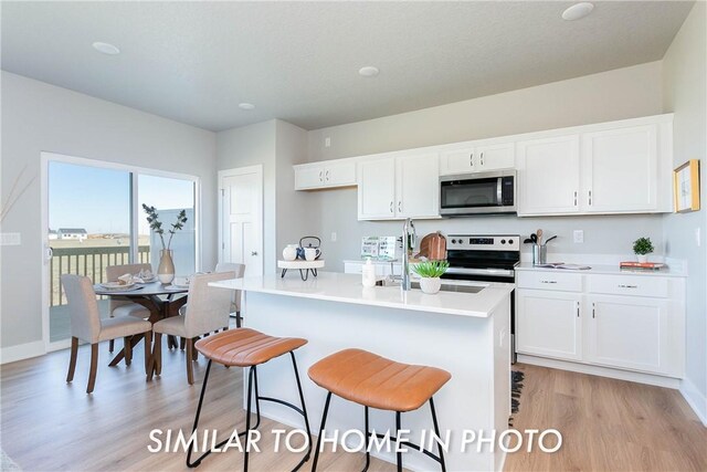 kitchen with white cabinetry, a breakfast bar area, a kitchen island with sink, stainless steel appliances, and light hardwood / wood-style floors