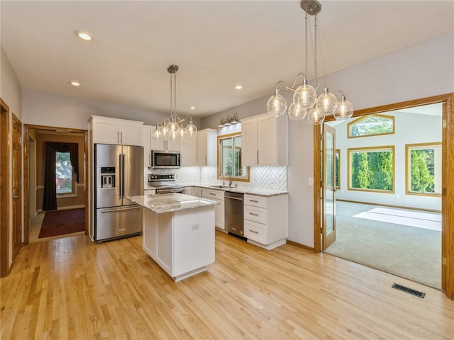 kitchen with a kitchen island, white cabinetry, a wealth of natural light, stainless steel appliances, and decorative light fixtures