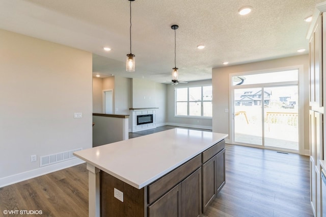 kitchen featuring visible vents, dark wood finished floors, a glass covered fireplace, light countertops, and pendant lighting