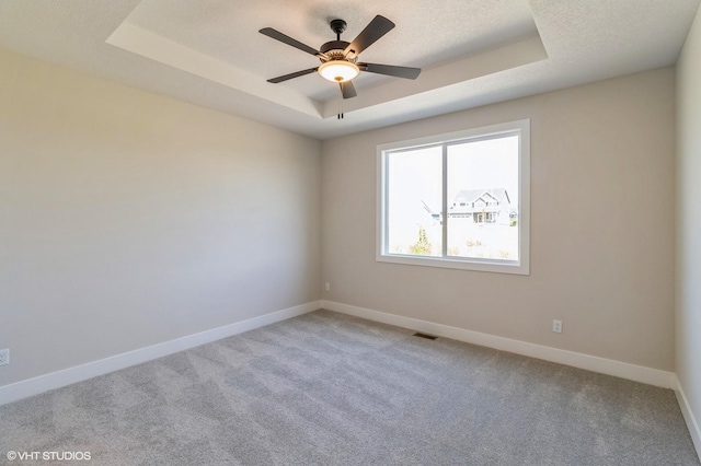 carpeted spare room featuring a textured ceiling, a tray ceiling, a ceiling fan, and baseboards