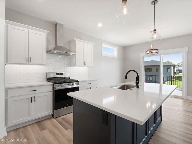 kitchen with hanging light fixtures, sink, stainless steel range with gas cooktop, wall chimney range hood, and white cabinetry