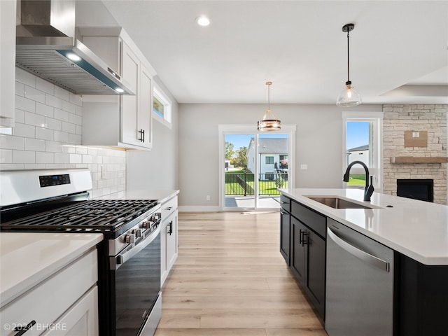 kitchen with white cabinetry, sink, appliances with stainless steel finishes, wall chimney exhaust hood, and hanging light fixtures