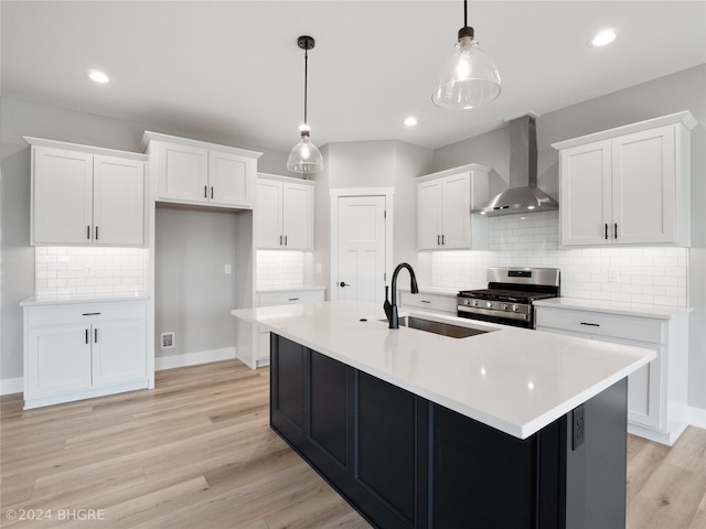 kitchen with white cabinetry, decorative light fixtures, stainless steel range with gas cooktop, sink, and wall chimney exhaust hood