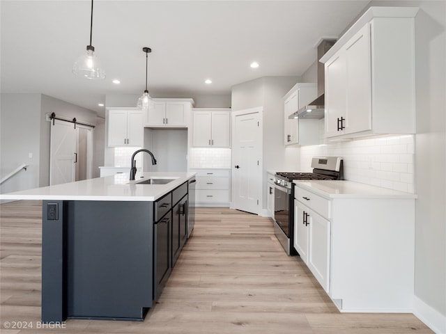 kitchen with stainless steel appliances, a barn door, decorative light fixtures, sink, and an island with sink