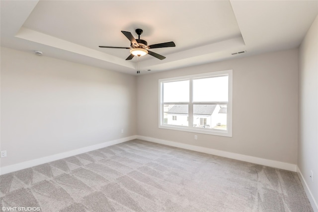 empty room with light colored carpet, a raised ceiling, and ceiling fan