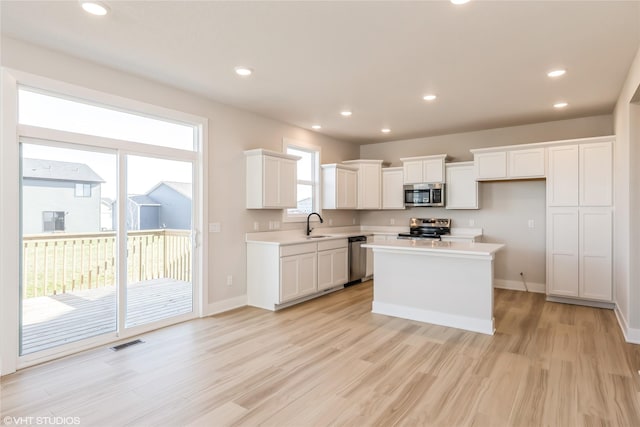 kitchen with white cabinetry, a center island, stainless steel appliances, and light hardwood / wood-style flooring