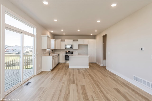 kitchen featuring stainless steel appliances, sink, white cabinets, light hardwood / wood-style floors, and a kitchen island