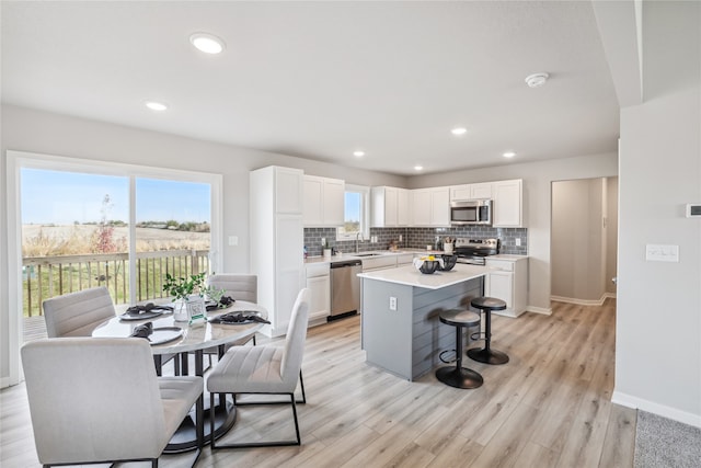 kitchen with light hardwood / wood-style flooring, decorative backsplash, a kitchen island, white cabinetry, and stainless steel appliances