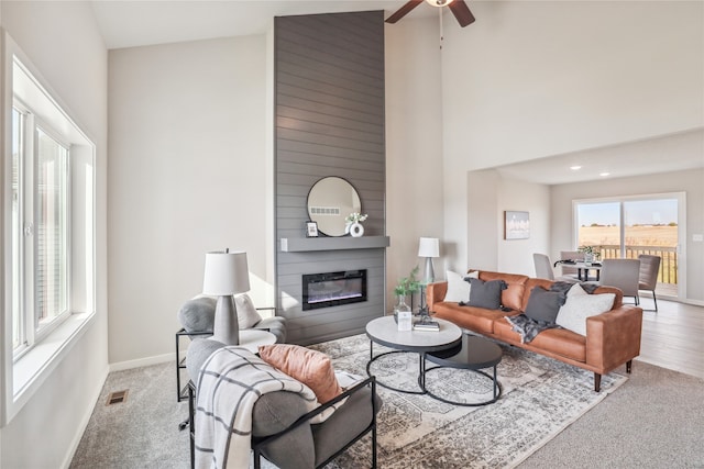 living room with ceiling fan, a fireplace, high vaulted ceiling, and light colored carpet