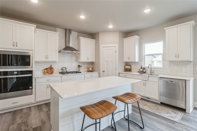 kitchen featuring wood-type flooring, sink, stainless steel appliances, wall chimney exhaust hood, and white cabinets