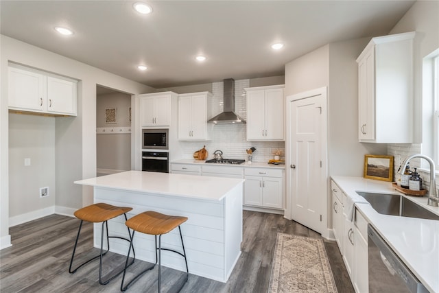 kitchen with a kitchen island, wall chimney range hood, sink, white cabinets, and appliances with stainless steel finishes