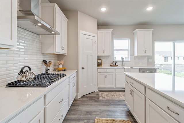 kitchen featuring wall chimney exhaust hood, stainless steel appliances, backsplash, hardwood / wood-style floors, and white cabinets