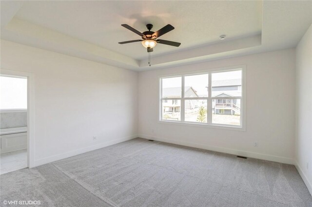 carpeted spare room with ceiling fan and a tray ceiling