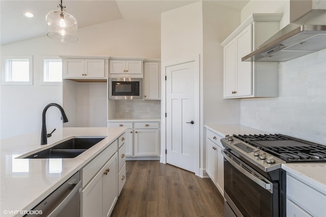 kitchen featuring wall chimney range hood, appliances with stainless steel finishes, white cabinetry, vaulted ceiling, and sink