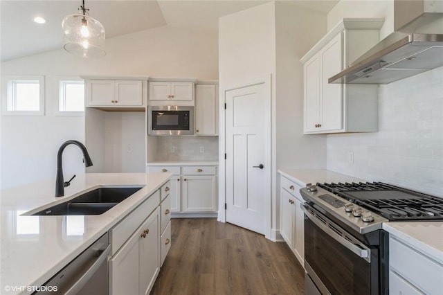 kitchen featuring wall chimney exhaust hood, sink, hanging light fixtures, appliances with stainless steel finishes, and white cabinets