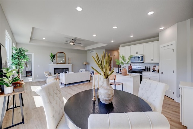 dining room with a tray ceiling, light hardwood / wood-style flooring, and ceiling fan