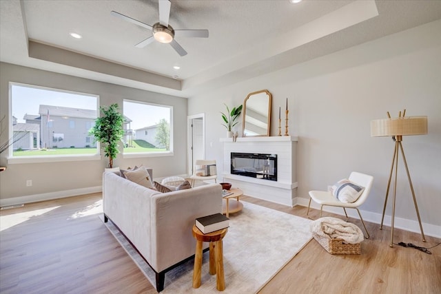 living room with a tray ceiling, ceiling fan, and light hardwood / wood-style flooring