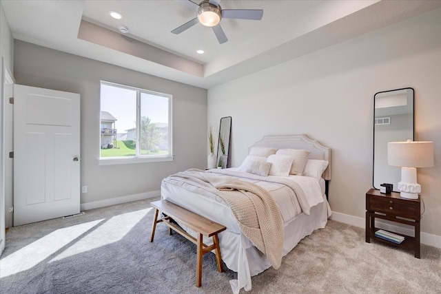 carpeted bedroom with a raised ceiling and ceiling fan