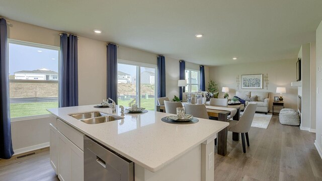 kitchen featuring sink, white cabinetry, a center island with sink, stainless steel dishwasher, and light hardwood / wood-style floors