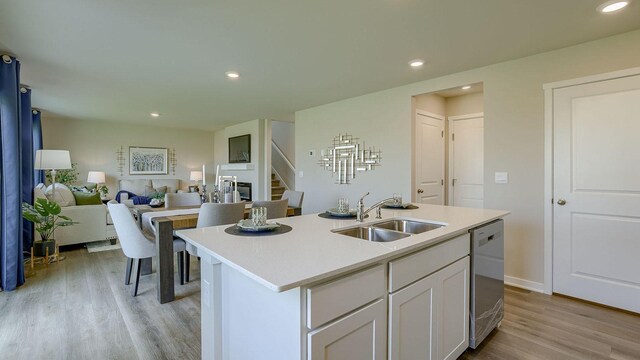 kitchen with sink, an island with sink, white cabinets, stainless steel dishwasher, and light wood-type flooring