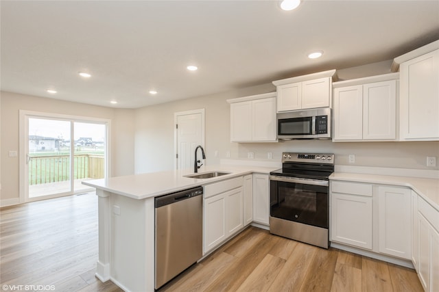 kitchen with kitchen peninsula, white cabinets, appliances with stainless steel finishes, light hardwood / wood-style flooring, and sink