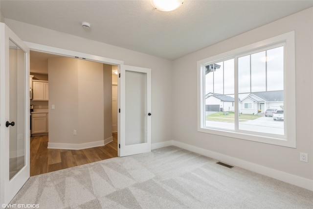 unfurnished bedroom with french doors, a textured ceiling, and light colored carpet