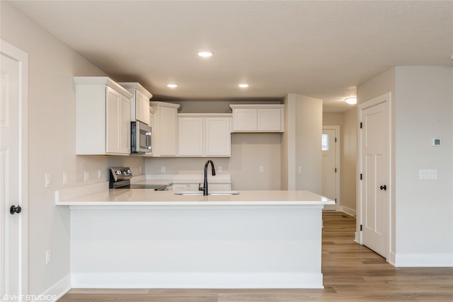 kitchen with light hardwood / wood-style flooring, kitchen peninsula, stainless steel appliances, sink, and white cabinetry