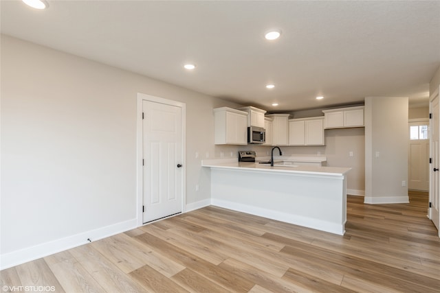 kitchen featuring kitchen peninsula, sink, white cabinetry, appliances with stainless steel finishes, and light hardwood / wood-style floors