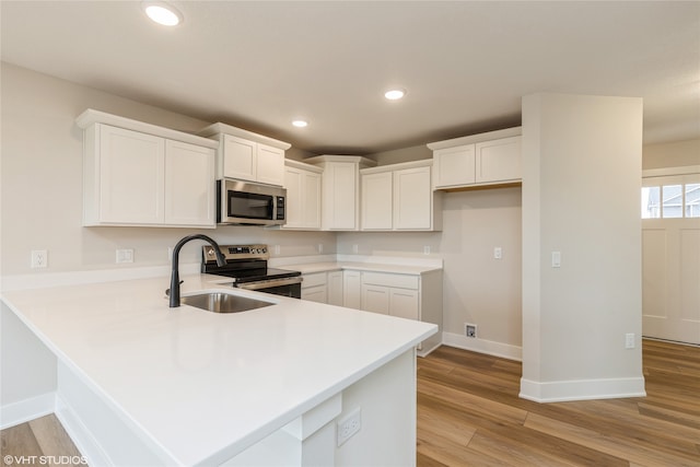 kitchen featuring appliances with stainless steel finishes, sink, kitchen peninsula, light hardwood / wood-style floors, and white cabinets