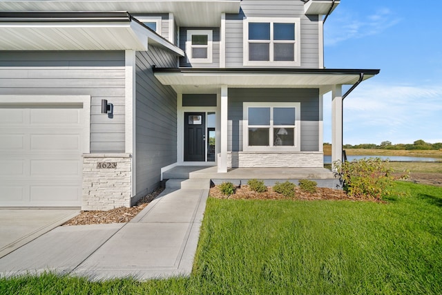 property entrance with covered porch, a water view, a garage, and a lawn