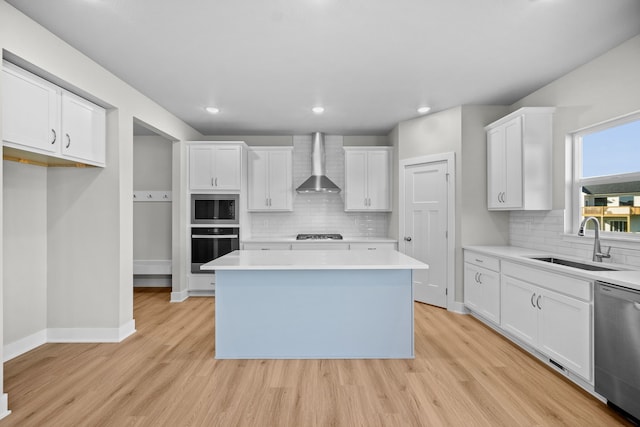 kitchen featuring wall chimney range hood, sink, appliances with stainless steel finishes, a kitchen island, and white cabinetry