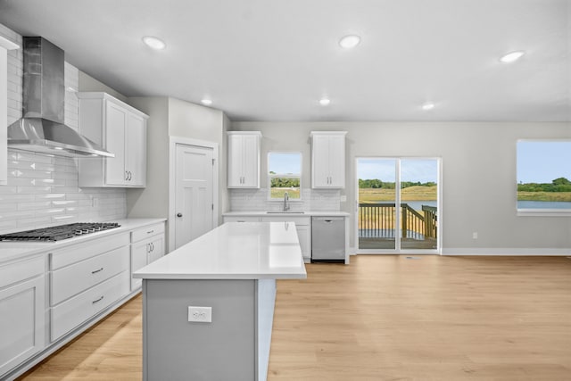 kitchen featuring appliances with stainless steel finishes, wall chimney range hood, white cabinets, light hardwood / wood-style floors, and a kitchen island