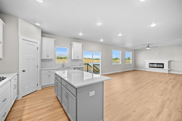 kitchen with light wood-type flooring, ceiling fan, sink, white cabinets, and a kitchen island