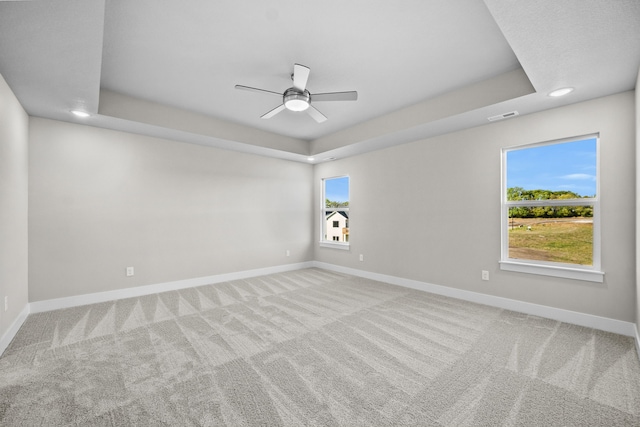 carpeted spare room with a raised ceiling and ceiling fan