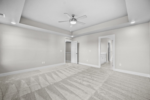 unfurnished bedroom with light carpet, connected bathroom, a tray ceiling, and ceiling fan