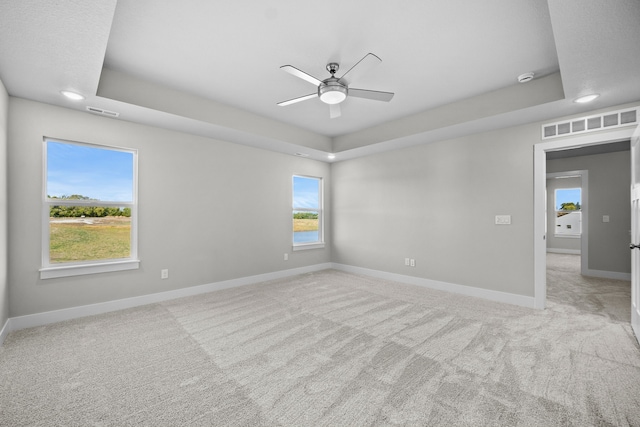 spare room featuring a tray ceiling, ceiling fan, and light colored carpet