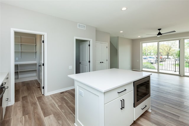 kitchen with light hardwood / wood-style flooring, ceiling fan, stainless steel microwave, white cabinetry, and a center island