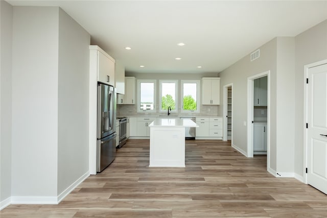 kitchen featuring appliances with stainless steel finishes, a kitchen island, tasteful backsplash, white cabinetry, and sink