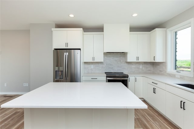 kitchen with a kitchen island, backsplash, stainless steel appliances, light hardwood / wood-style floors, and white cabinets