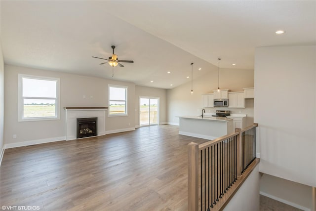 living room featuring ceiling fan, sink, light hardwood / wood-style flooring, and vaulted ceiling