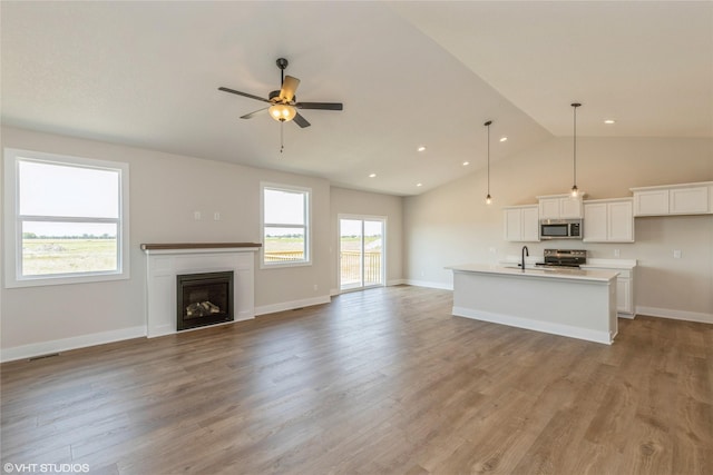 kitchen featuring an island with sink, pendant lighting, vaulted ceiling, appliances with stainless steel finishes, and light wood-type flooring