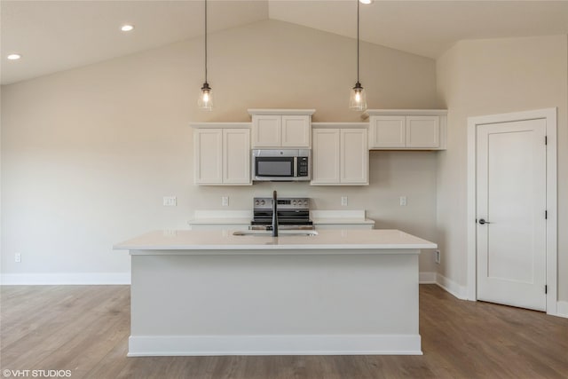 kitchen with decorative light fixtures, stainless steel appliances, an island with sink, and vaulted ceiling