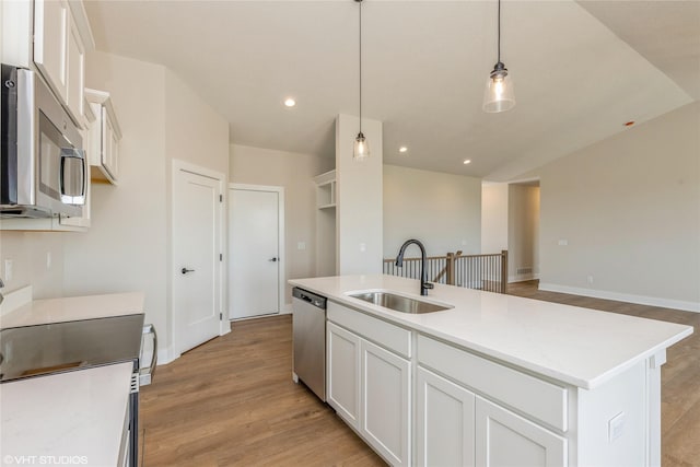 kitchen with sink, stainless steel appliances, an island with sink, pendant lighting, and light wood-type flooring