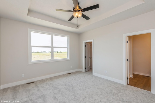 unfurnished bedroom featuring a tray ceiling, ceiling fan, and light colored carpet