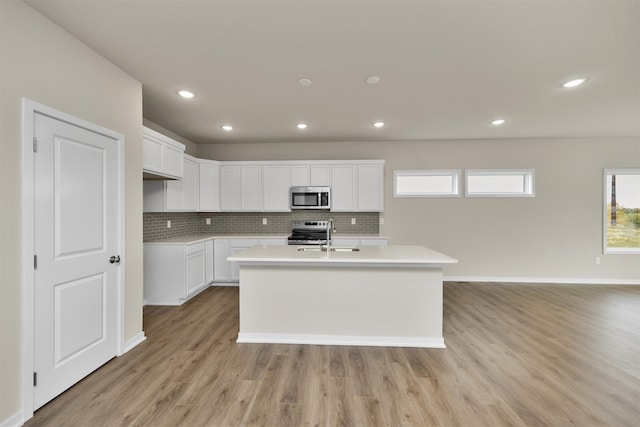 kitchen with a kitchen island with sink, light hardwood / wood-style flooring, stainless steel appliances, backsplash, and white cabinetry