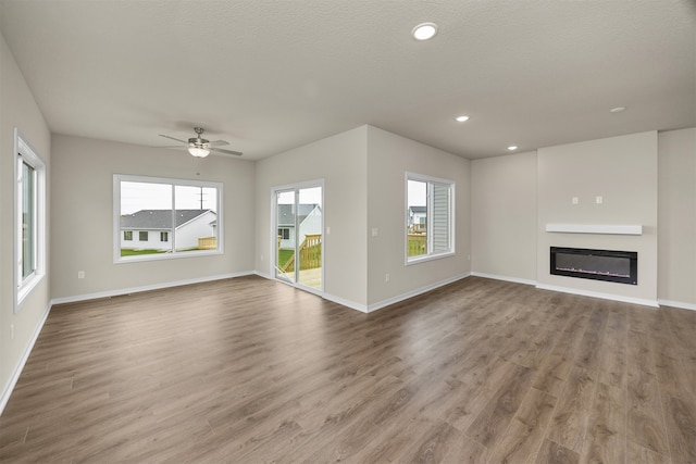 unfurnished living room with light hardwood / wood-style floors, a textured ceiling, a wealth of natural light, and ceiling fan