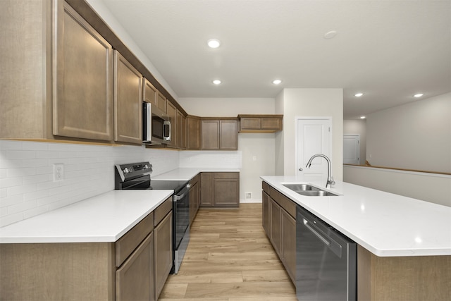 kitchen with appliances with stainless steel finishes, sink, light hardwood / wood-style floors, decorative backsplash, and a kitchen island with sink