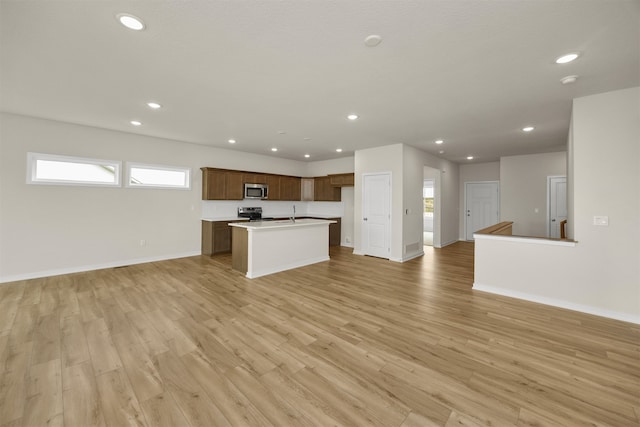 kitchen with appliances with stainless steel finishes, light hardwood / wood-style flooring, and a kitchen island with sink